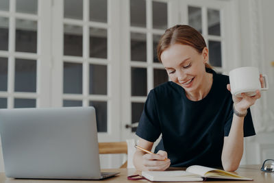 Young woman using phone while sitting on table