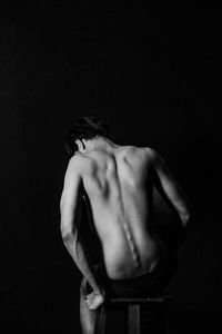 Rear view of shirtless man standing against black background