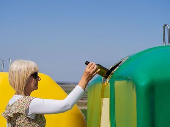 Rear view of woman holding yellow umbrella against blue sky