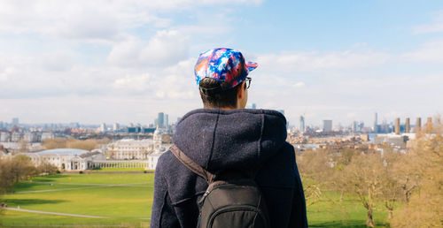 Rear view of man wearing cap while standing against field in city