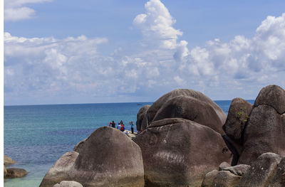 People on rocks by sea against sky