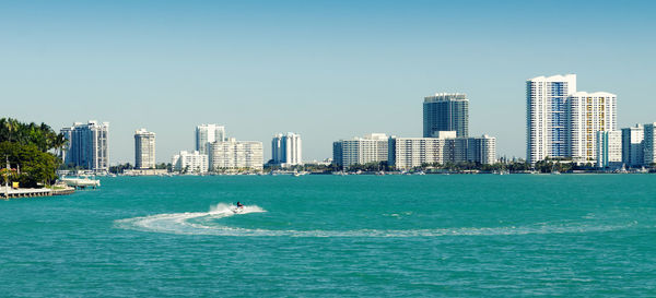 Woman riding jet ski on sea with city in background