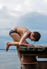 Side view of a boy climbing on bridge by sea against sky