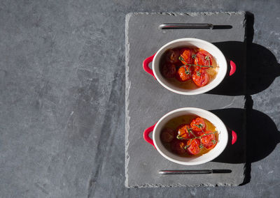 Baked cherry tomatoes in portioned saucepans in the sunlight on the table, flat lay, copy space