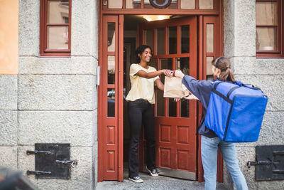 Food delivery woman delivering package to customer standing at doorway in city