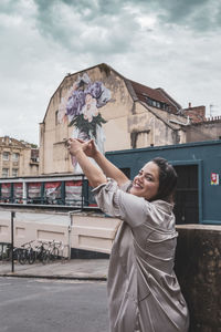 Happy young woman standing by building in city against sky