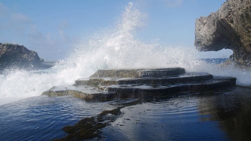 Waves splashing on rocks against sky