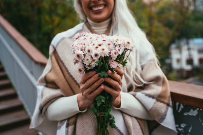 Midsection of woman holding flower bouquet standing outdoors