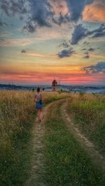 Rear view of people walking on field against sky during sunset