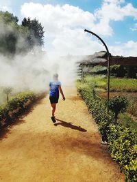 Rear view of man walking on road against sky