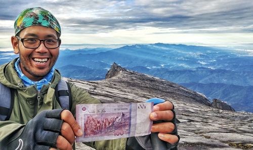 Portrait of smiling man holding money against mountains