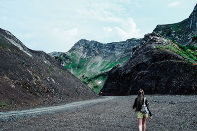 Rear view of woman walking on road against mountain range