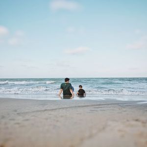Surface level view of father and son sitting at beach against sky