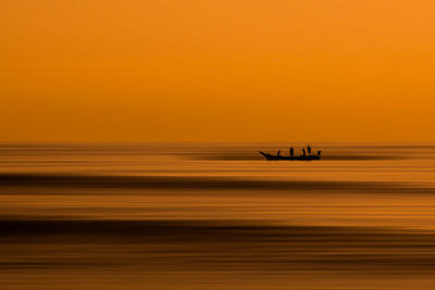 Silhouette boat on sea against orange sky