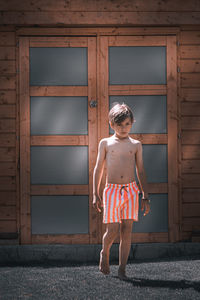 Full length portrait of boy standing against door