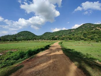 Dirt road amidst green landscape against sky