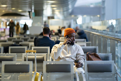 African traveler man drinking coffee waiting for flying at airport terminal, talking on cellphone.