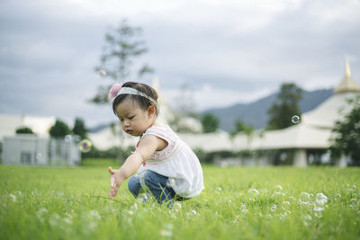 Side view of cute baby girl crouching on grassy land