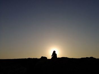 Silhouette woman sitting on rock against sky during sunset