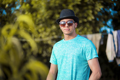 Portrait of young man wearing sunglasses standing against plants