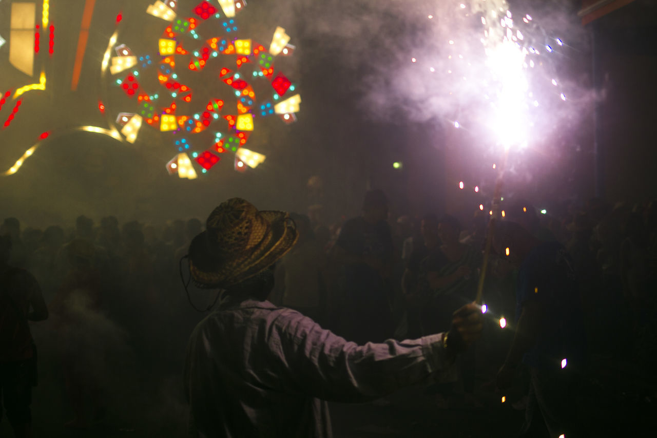 illuminated, celebration, real people, event, night, arts culture and entertainment, enjoyment, leisure activity, lifestyles, people, standing, hat, glowing, men, women, indoors, crowd, group of people, rear view, festival, light