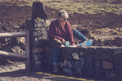 Senior woman sitting on stone wall while looking at map