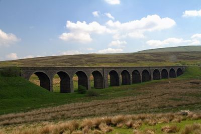 Arch bridge on field against sky