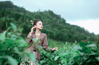 Young woman looking away against trees