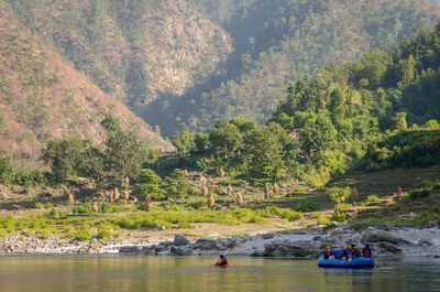 People on river by trees against mountains