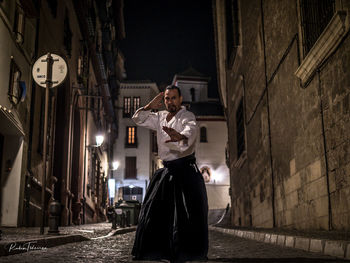 Man standing on illuminated street amidst buildings at night