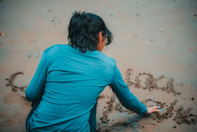 Rear view of woman crouching and writing in the sand