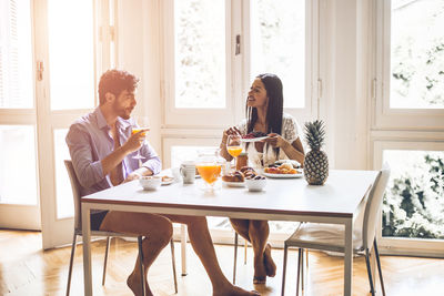 Happy couple having breakfast while sitting at dining table