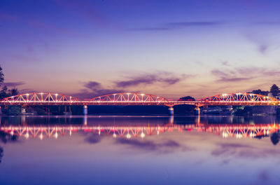 Illuminated bridge over river against sky at night