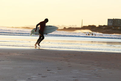 Man carrying surfboard on shore at beach