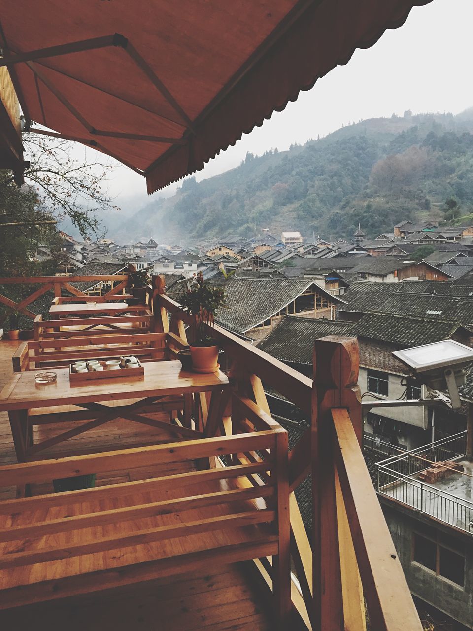 built structure, architecture, building exterior, roof, railing, house, mountain, sky, residential structure, residential building, balcony, high angle view, sunlight, town, city, tree, steps, day, residential district, chair