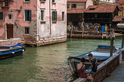 People sitting on boat in canal along buildings