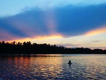 Silhouette man swimming in lake against sky during sunset