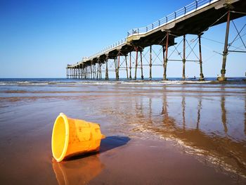 Peir and bucket on beach against clear sky