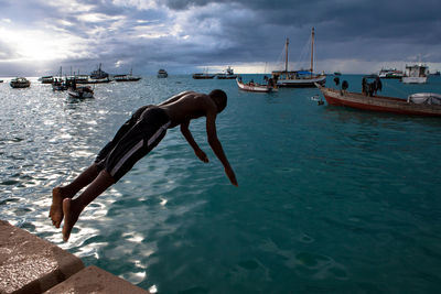 Shirtless man diving into sea against cloudy sky