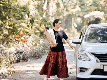 A woman hold a paper bag of dry flower and back to car after shopping