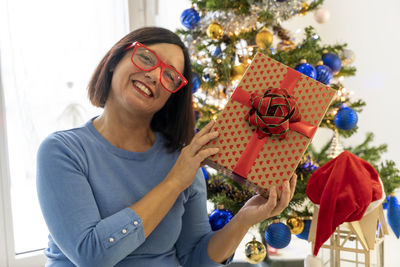 Portrait of woman holding christmas tree at home