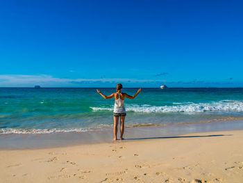 Rear view of young woman standing at beach against clear blue sky