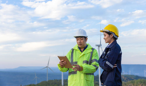Engineers using digital tablet standing against wind turbine
