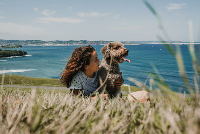 Happy woman with dog on field against sea