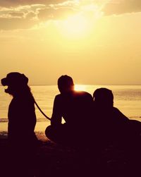 Silhouette people sitting on beach against sky during sunset