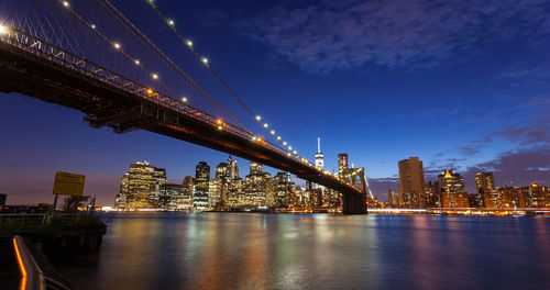 Illuminated bridge over river by buildings against sky at night