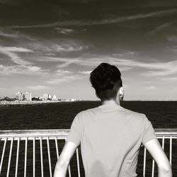 Rear view of man standing by railing against sea