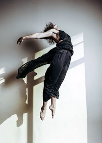 Side view of woman jumping against wall