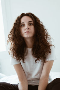 Portrait of beautiful woman with curly hair sitting against wall