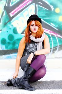 Full length portrait of young woman sitting against graffiti wall